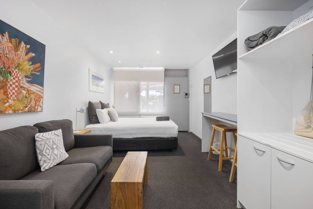 Quarto de hotel moderno com cama, sofá, banco de madeira e escrivaninha.