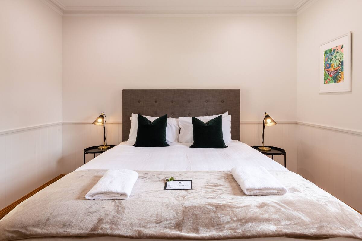 A neatly made bed with a grey headboard, two black pillows, and two bedside lamps.