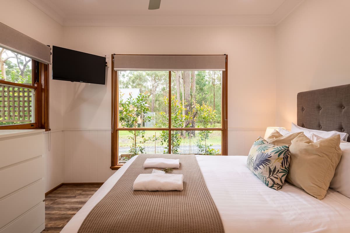 A bedroom with a large window, a flat-screen TV, a bed with white linens, and a grey headboard.