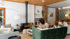 A modern living room with a fireplace, green sofa, and a dining area with a brick wall and wooden ceiling. - Bay and Bush, Jervis Bay (Woollamia)