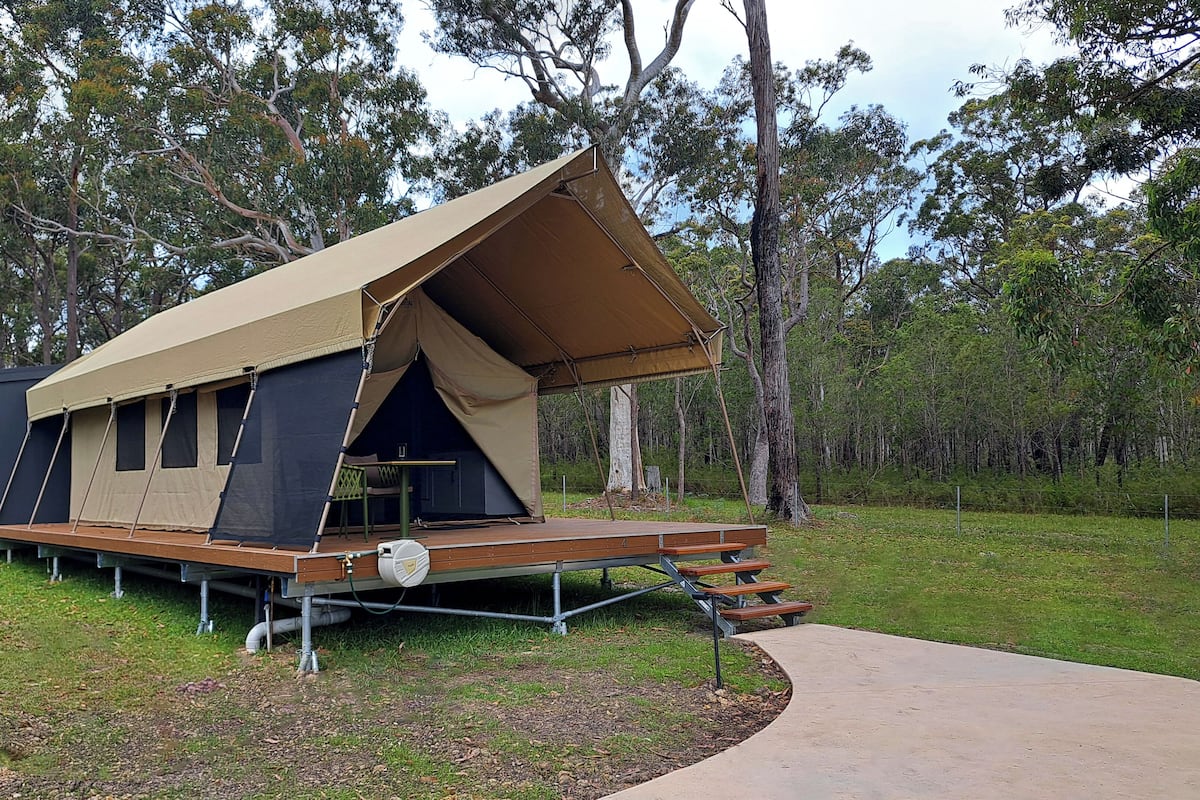 A camping site with a large tent structure, a small cabin, and a concrete pathway.