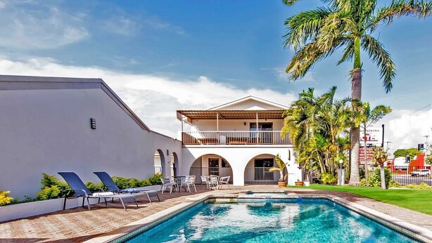 A two-story building with a pool, outdoor seating, and palm trees. - Casa Nostra Motel Mackay (West Mackay)