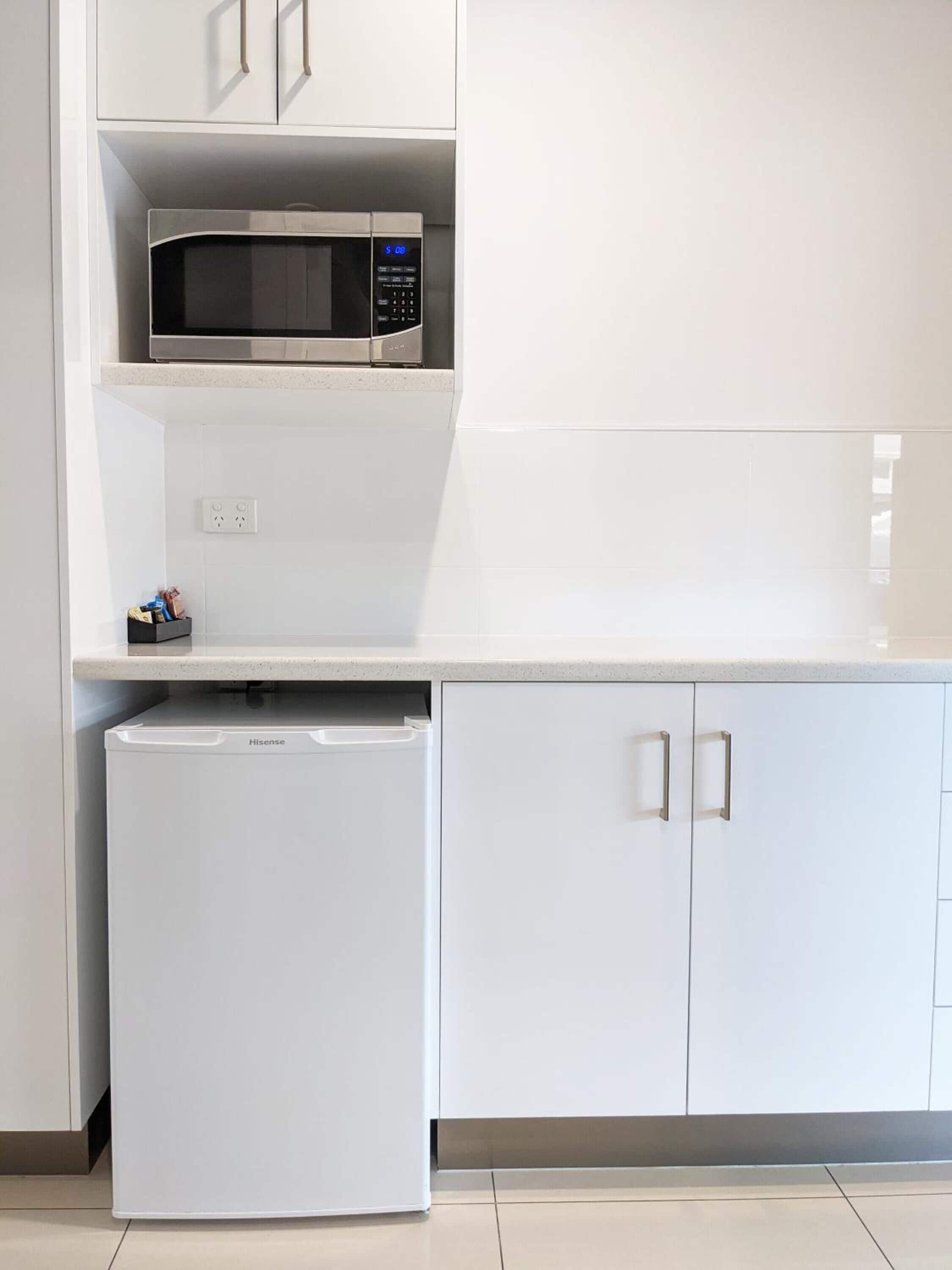 A compact kitchen with a microwave, a small refrigerator, and white cabinetry.