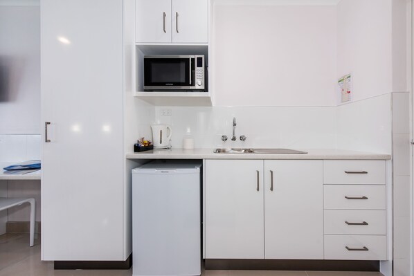 A modern kitchen with white cabinets, a microwave, a coffee maker, and a dishwasher. - Casa Nostra Motel Mackay (West Mackay)