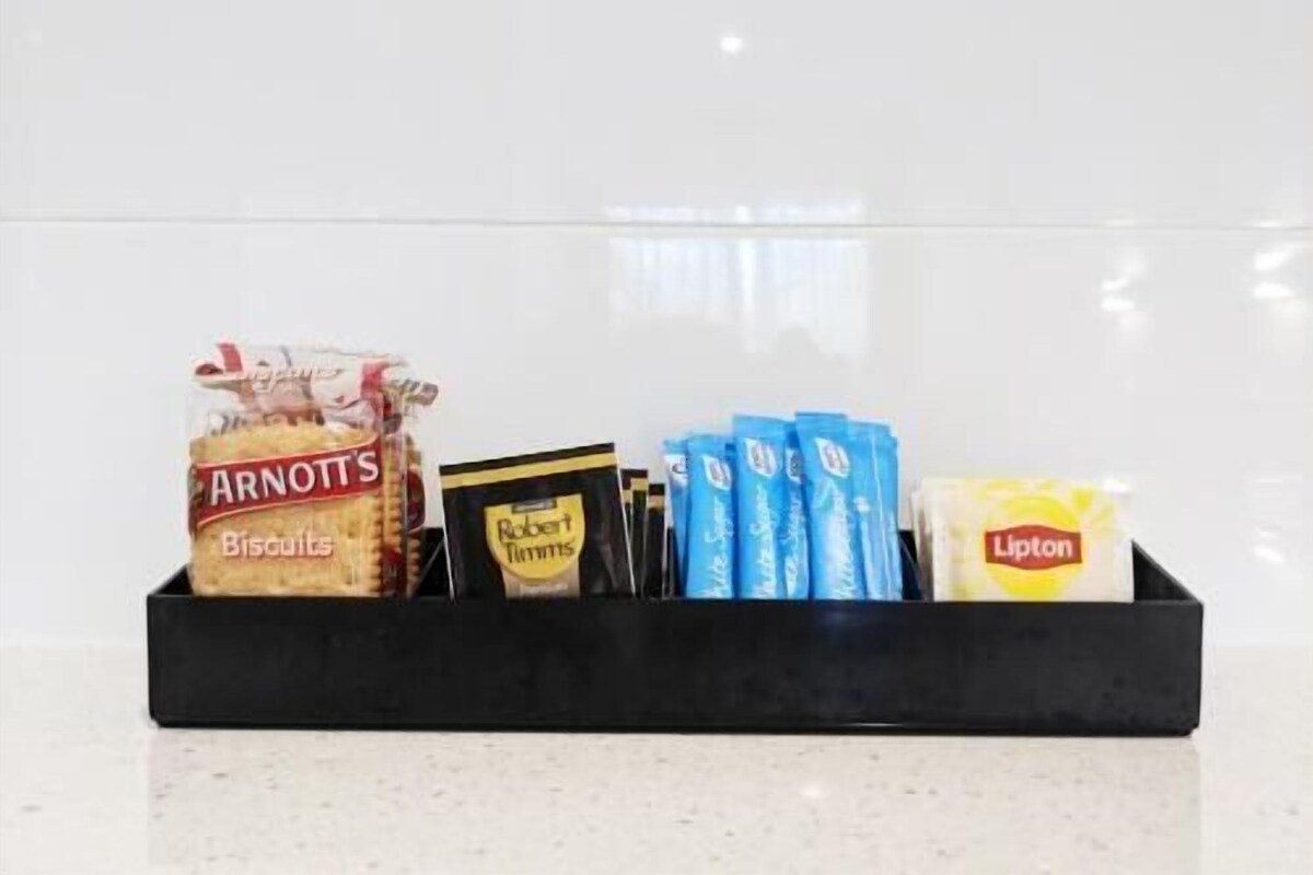 Una bandeja negra con diversos productos alimenticios envasados, incluyendo galletas Arnott’s, patatas fritas Robert’s y té Lipton.