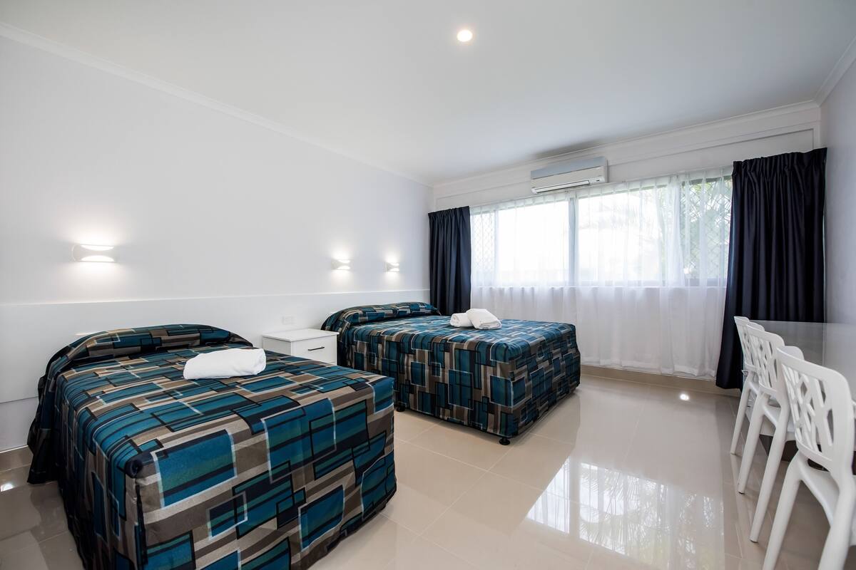 A hotel room with two beds, a desk, and a dining area with chairs.