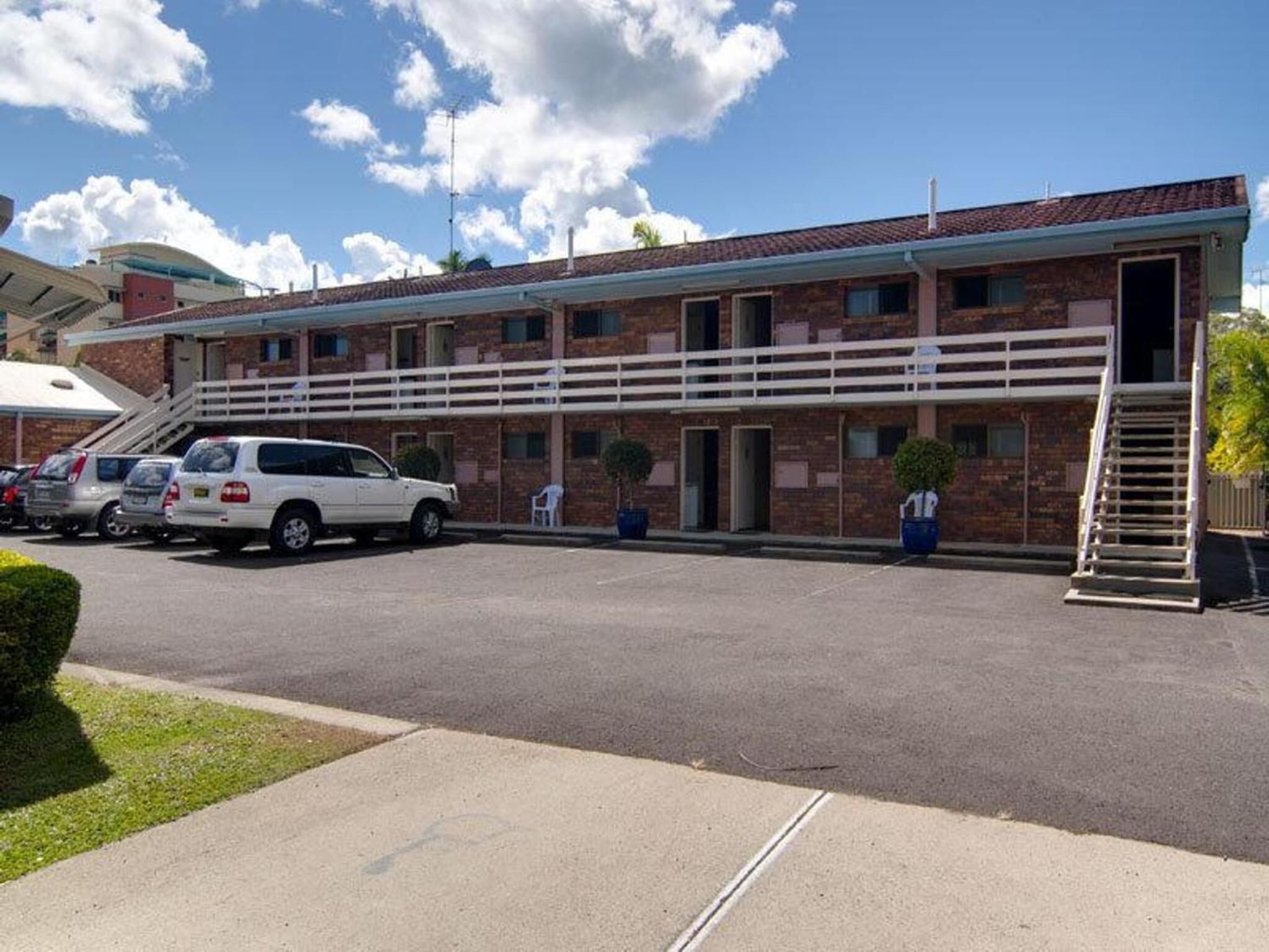 Un motel de dos pisos con fachada de ladrillo, una zona de estacionamiento techada y una escalera que conduce a la entrada.