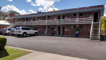 Un motel de dos pisos con fachada de ladrillo, una zona de estacionamiento techada y una escalera que conduce a la entrada.