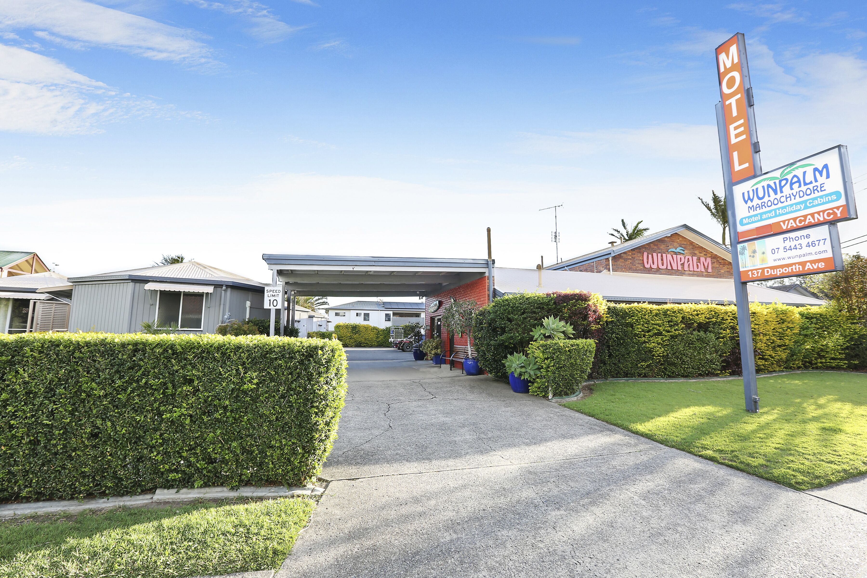 A motel with a clear driveway leading to the entrance, a speed limit sign, and a signboard advertising the motel and its vacancy status.