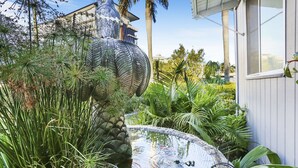Een tuin met een vijver, een groot decoratief beeld en weelderige begroeiing.