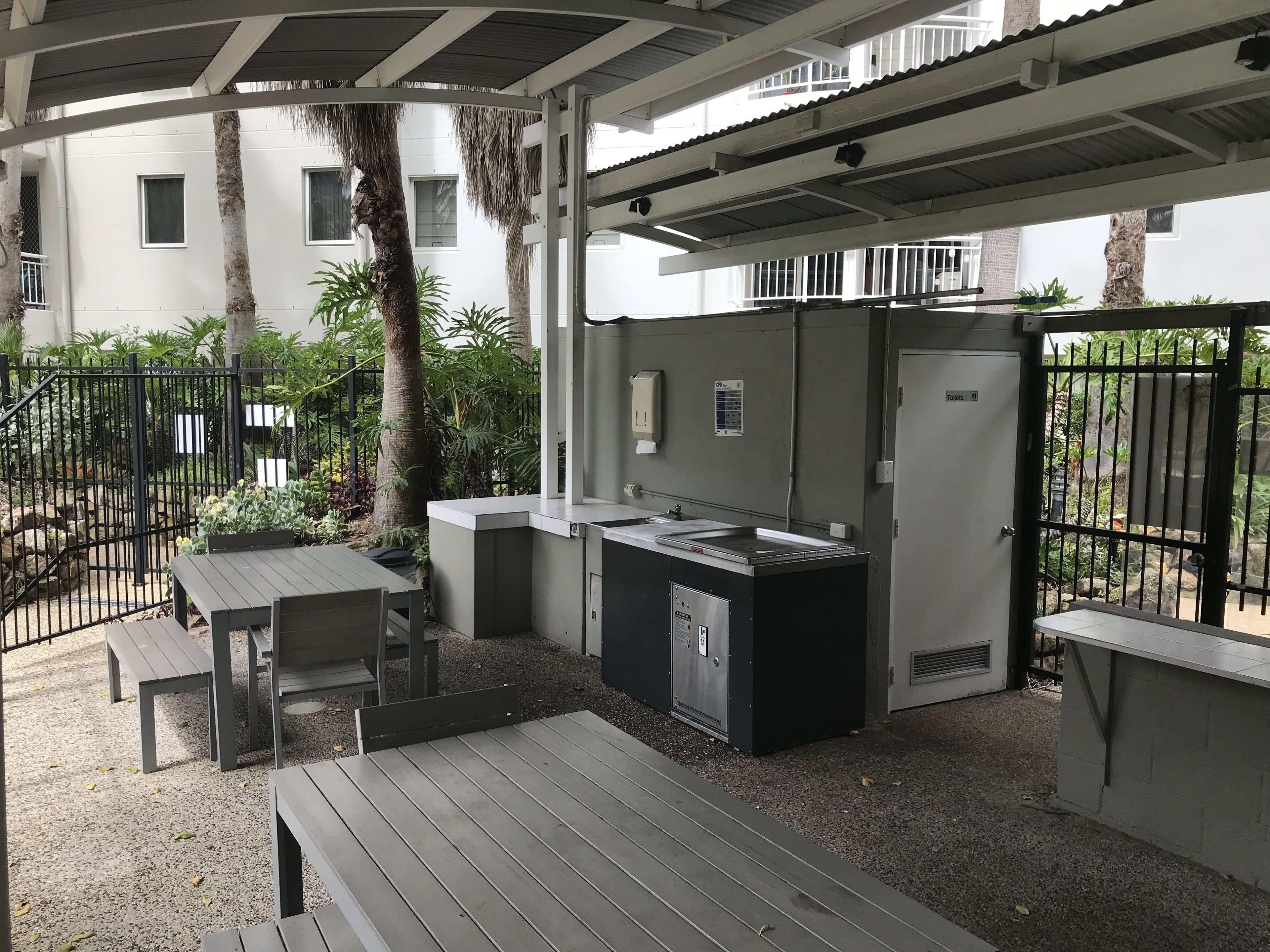 An outdoor patio area with a grill station, seating, and a view of a building in the background.