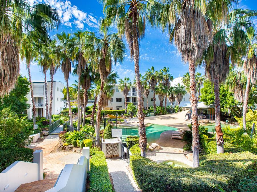 A resort with palm trees, a pool, and a pathway leading to a building.