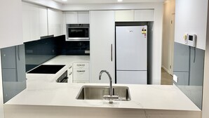 A modern kitchen with white cabinets, a stainless steel sink, a built-in microwave, and a refrigerator. - Bridgewater Terraces (Kangaroo Point)
