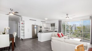 A modern kitchen with white cabinets, a central island, and a dining area with a white table and chairs. - Bridgewater Terraces (Kangaroo Point)