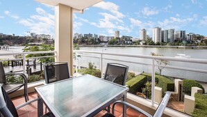 A balcony with a glass table and chairs, overlooking a river and cityscape. - Bridgewater Terraces (Kangaroo Point)