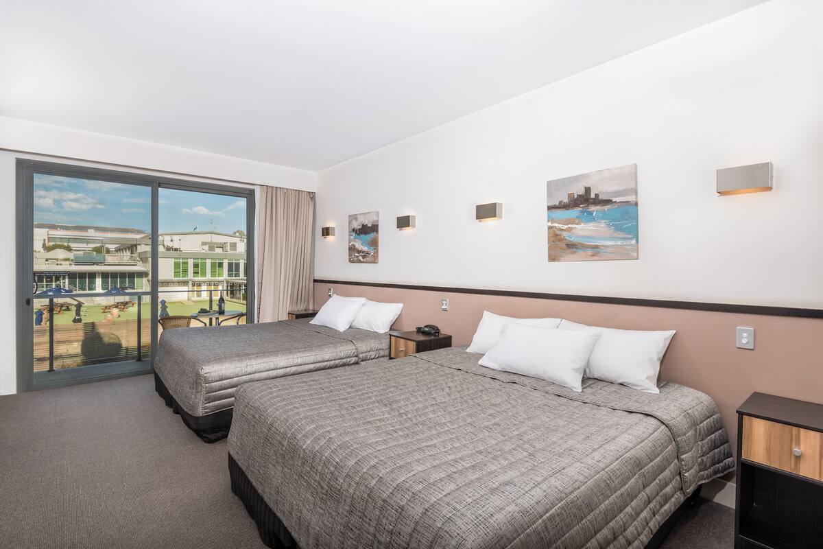 A hotel room with two beds, a balcony with a view of buildings, and artwork on the walls.
