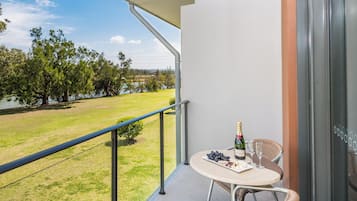 A balcony with a table set for two, overlooking a grassy area and a body of water.