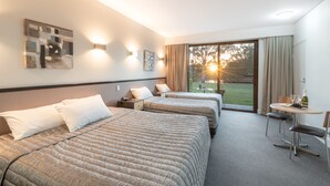 A hotel room with two beds, a small table with a bottle and glasses, and a view of the outdoors. - Macquarie 4 Star (Argenton)