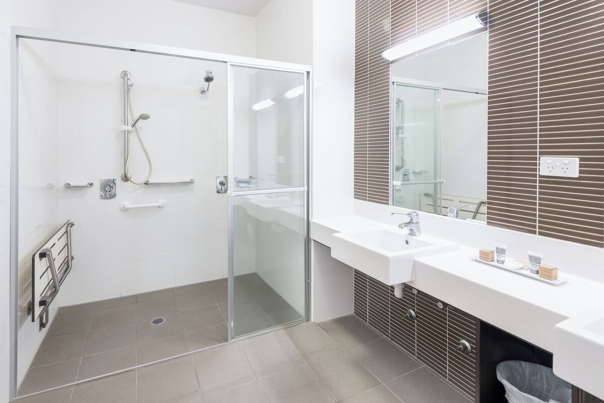 A modern bathroom with a glass-enclosed shower, a white sink with a mirror, and a brown tiled wall.