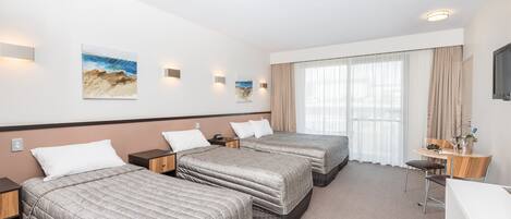 Een hotelkamer met drie bedden, een bureau en een stoel. Er zijn wandlampen en kunstwerken.