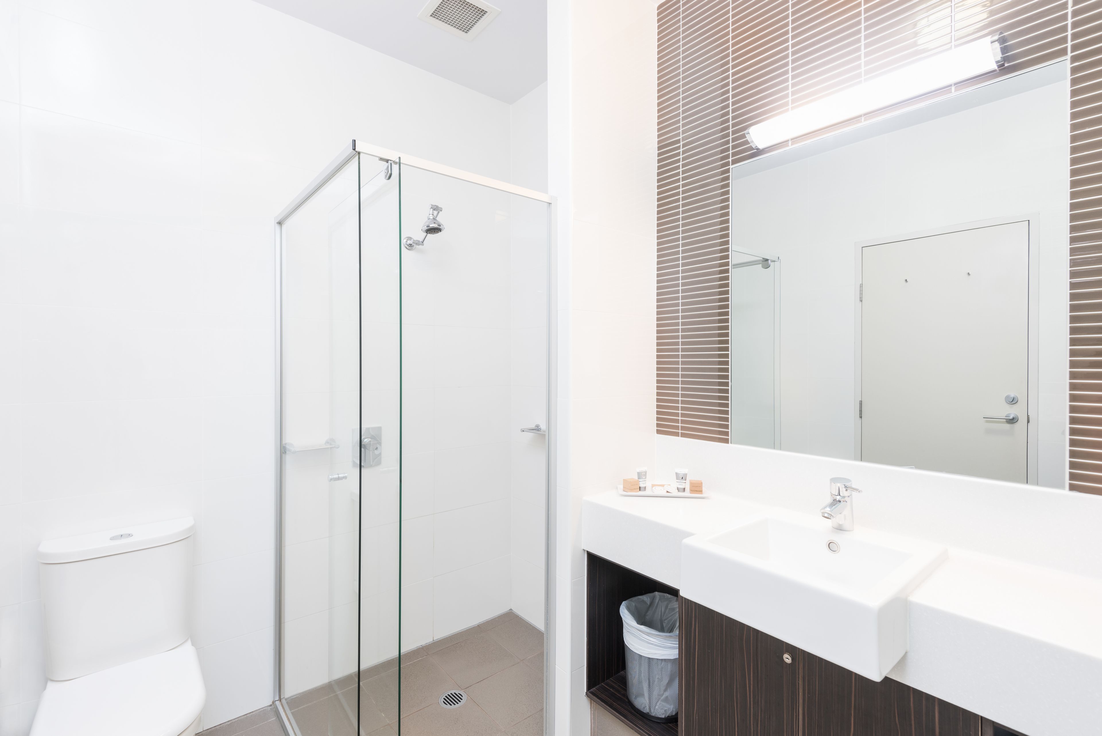 Een moderne badkamer met een douchecabine van glas, een witte wastafel en een grote spiegel.