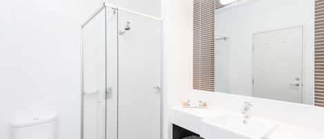 Un bagno moderno con box doccia in vetro, lavandino bianco e uno specchio grande.