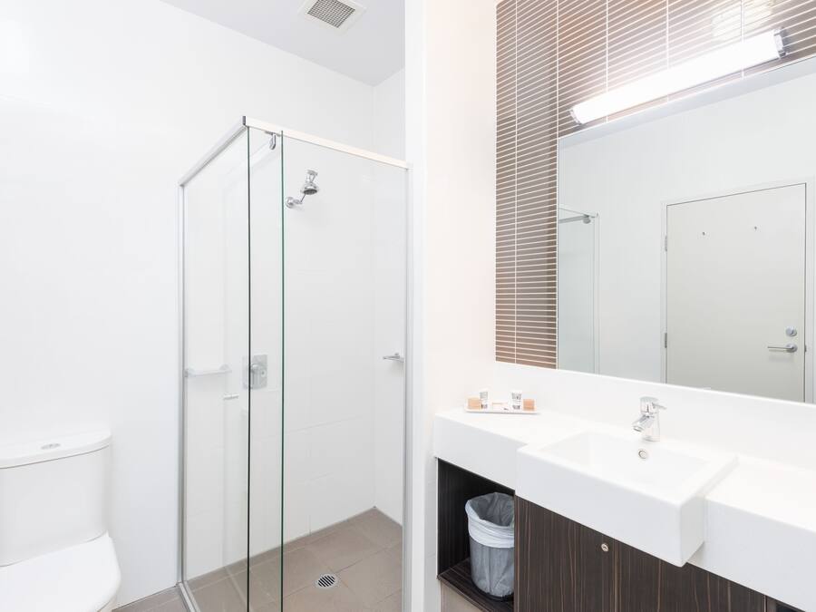 Un baño moderno con cabina de ducha de vidrio, un lavamanos blanco y un espejo grande.