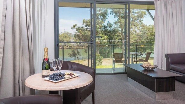 A modern room with a balcony, a round table with a bottle of champagne, glasses, and a plate of grapes. - Macquarie 4 Star (Argenton)