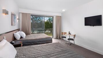 A hotel room with two beds, a desk with a chair, a flat-screen TV, and a large window with curtains.