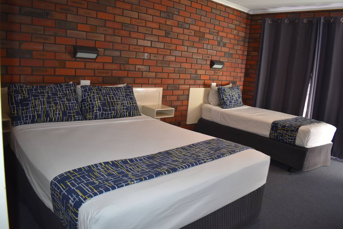 A hotel room with two beds, a brick wall, and a curtain.