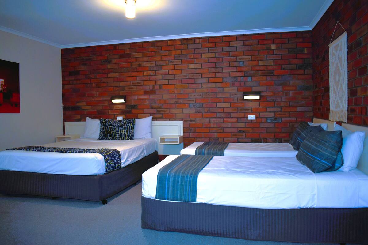 A hotel room with two beds, a brick-patterned wall, and a ceiling light fixture.