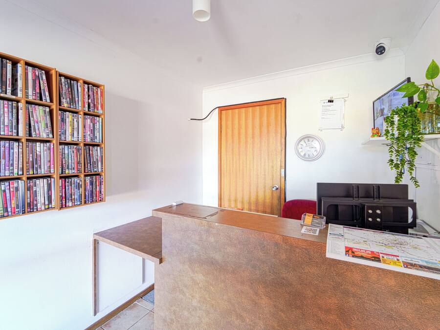 Una habitación con una estantería de madera llena de libros, un mostrador de recepción de madera, una puerta, un reloj en la pared y una planta en maceta.