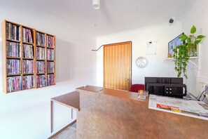 Une pièce comprenant une bibliothèque en bois remplie de livres, un comptoir d’accueil en bois, une porte, une horloge murale et une plante en pot.