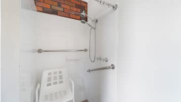 Un espace douche avec un mur recouvert de carreaux blancs, un mur d’accent en briques et une chaise en plastique blanche.