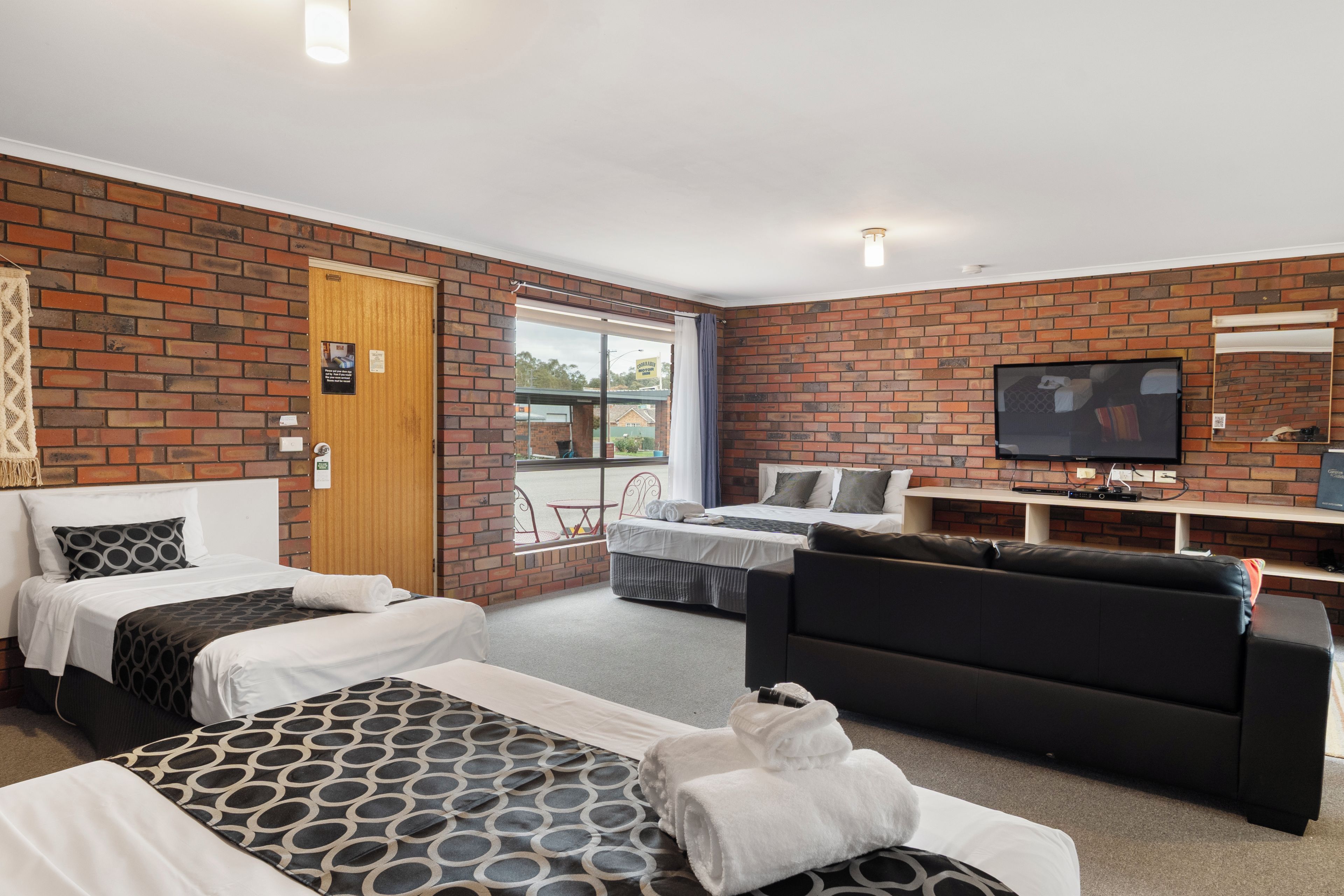A hotel room with two beds, a sofa, a television, and a brick wall.