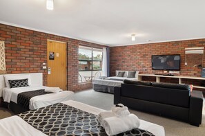 Une chambre d’hôtel avec deux lits, un canapé, une télévision et un mur en briques.