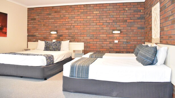 A hotel room with two beds, a brick wall, and two bedside tables with lamps.