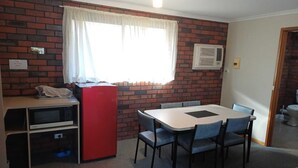 A compact kitchen with a red refrigerator, a microwave, and a sink. There's a dining table with chairs and a window with curtains.