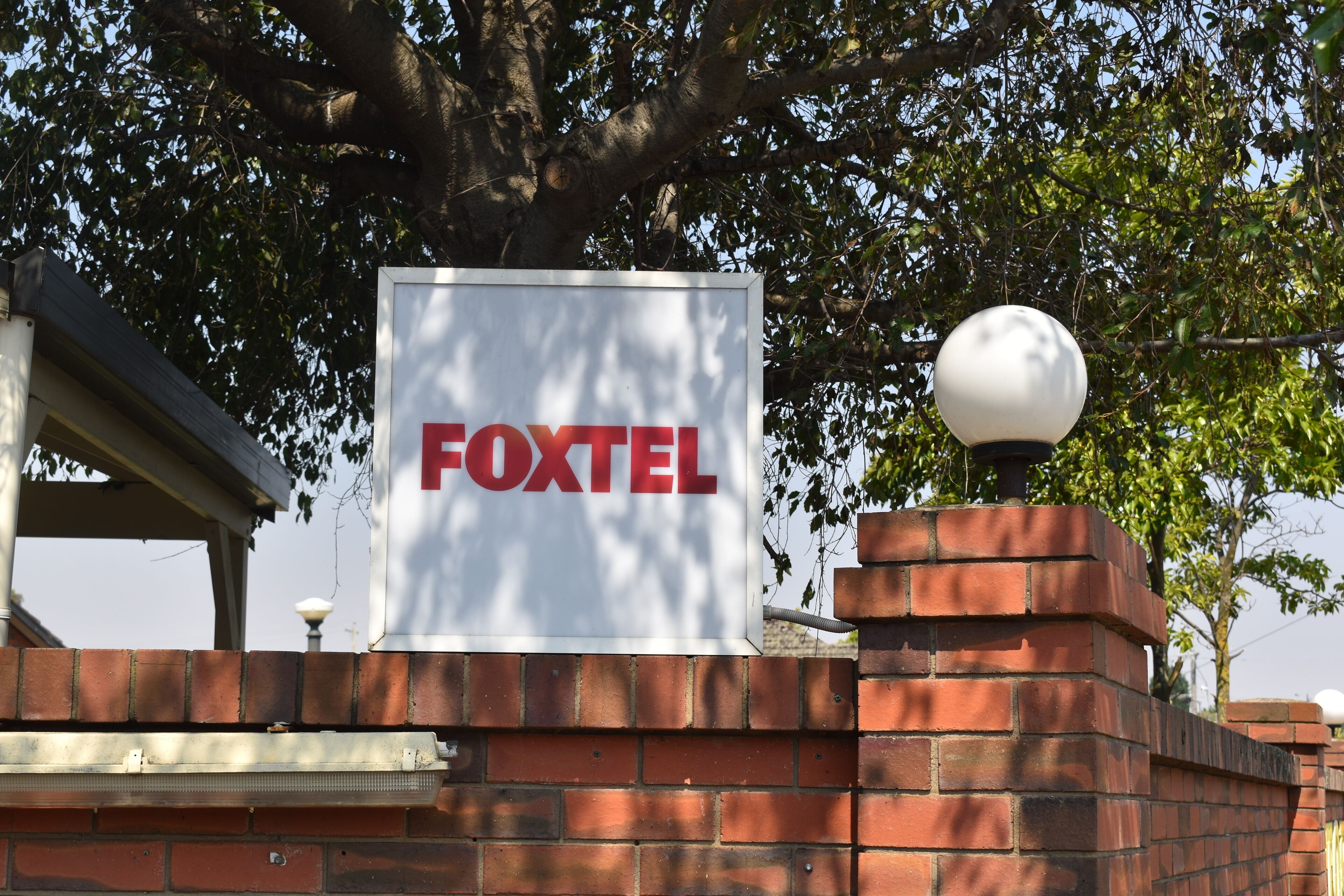 Un letrero de 'FOXTEL' en una pared de ladrillo, con un farol cercano.