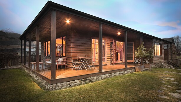 A wooden cabin with a covered porch, stone foundation, and outdoor seating area. - Glenorchy Lake House (Glenorchy)