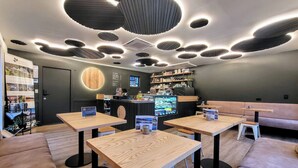 A modern cafe with wooden tables and black chairs, a counter with a menu display, and a wall with a circular wooden design. - Glenorchy Lake House (Glenorchy)