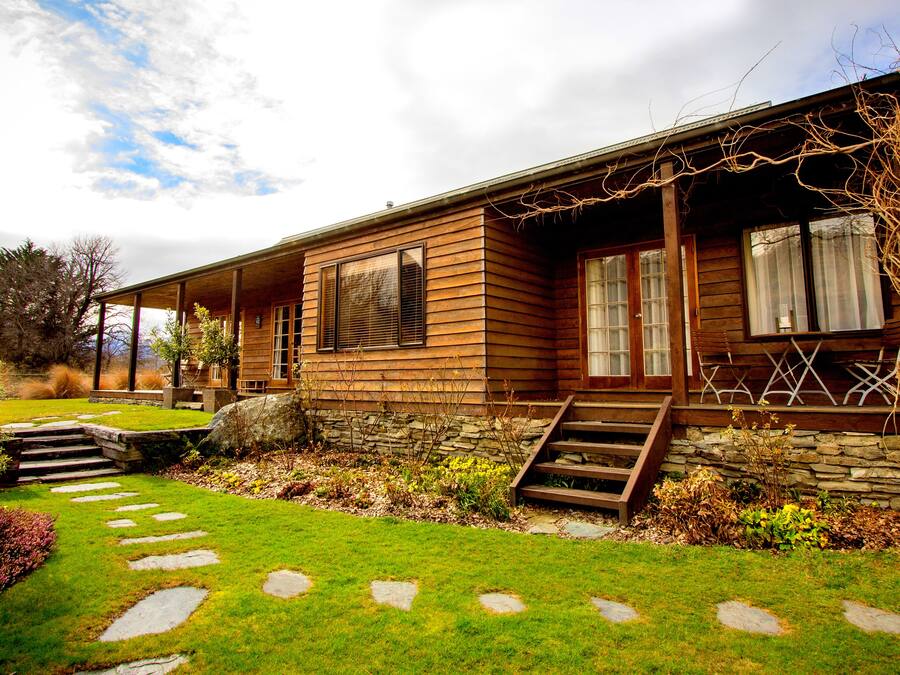 Une maison en bois avec des fondations en pierre, un porche couvert et un chemin en pierre menant à l’entrée.