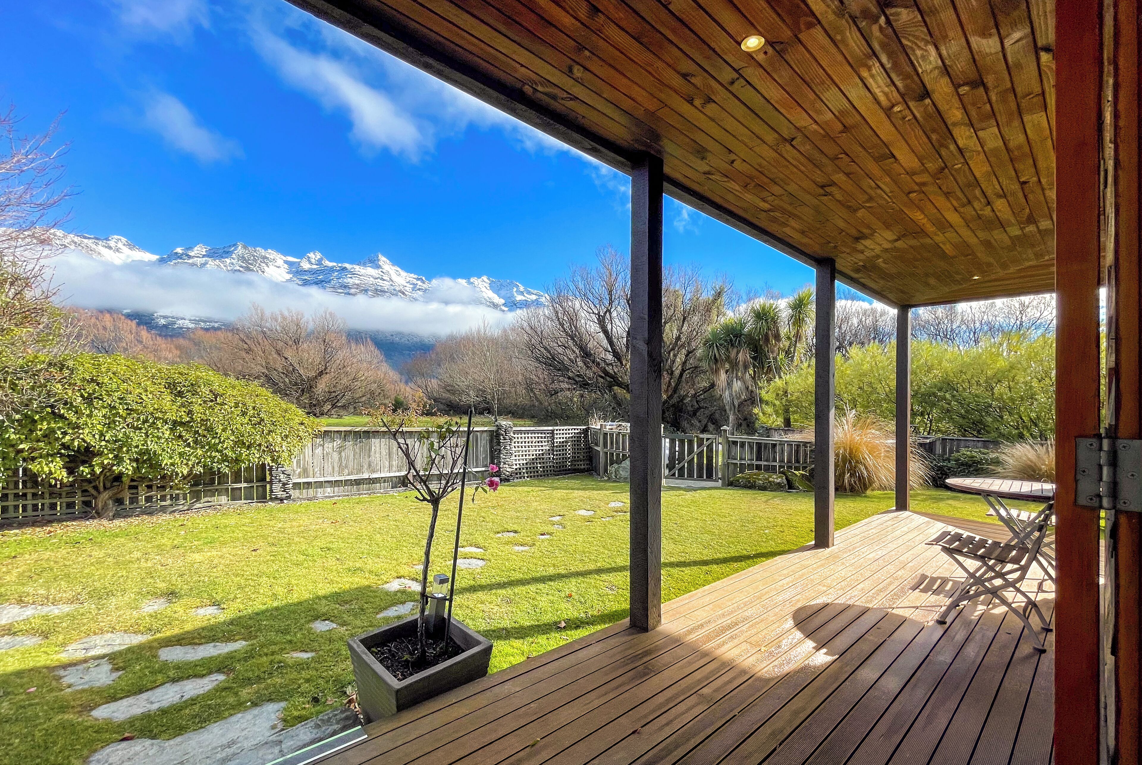 A wooden deck with a view of snow-capped mountains and a grassy yard.