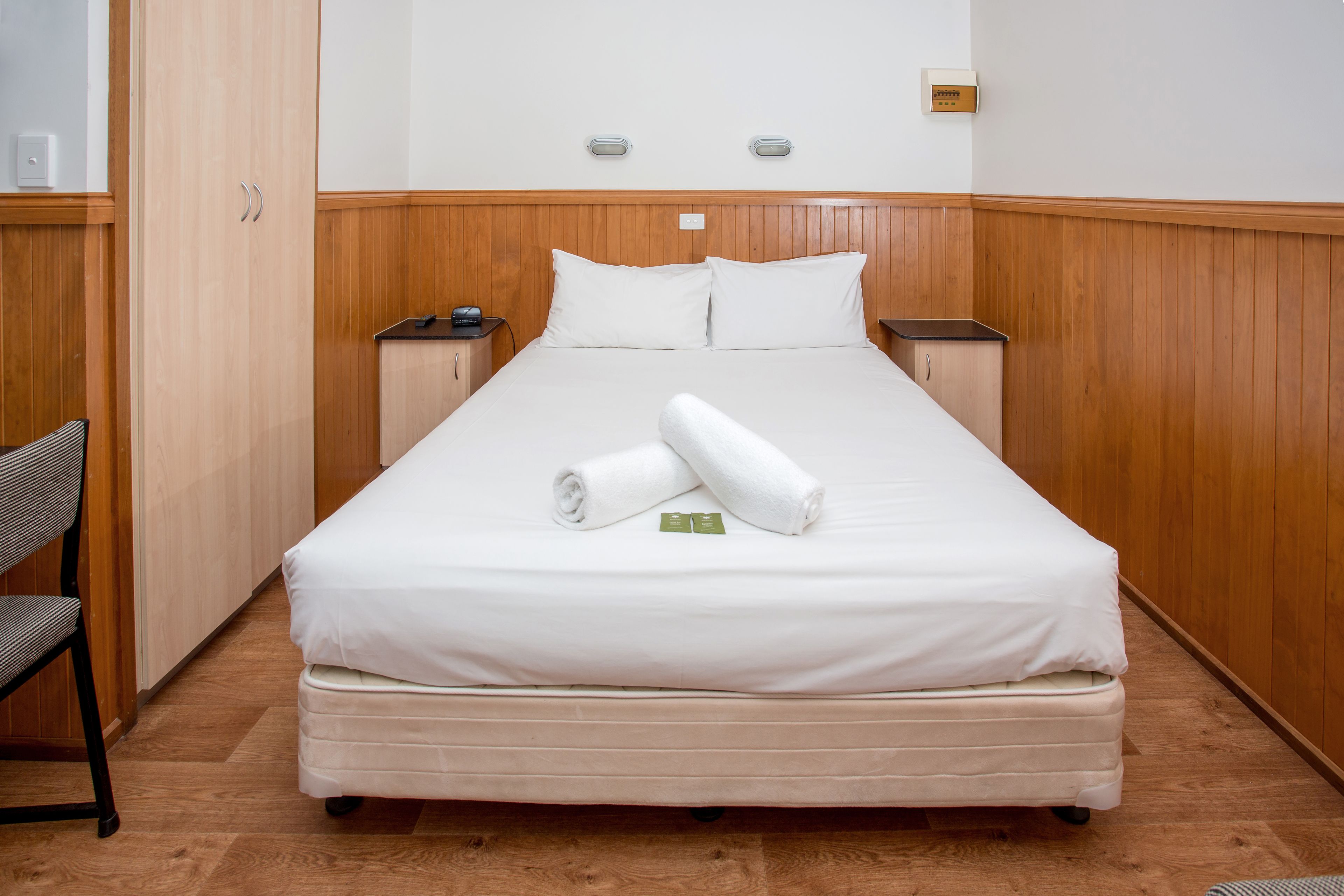A neatly made bed with white linens, two bedside tables, and a wooden headboard.
