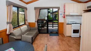A compact kitchen with a dining area, a sofa, and a large window with curtains. - Big4 Shepparton Park Lane (Kialla)
