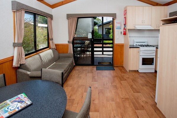 A compact kitchen with a dining area, a sofa, and a large window with curtains. - Big4 Shepparton Park Lane (Kialla)
