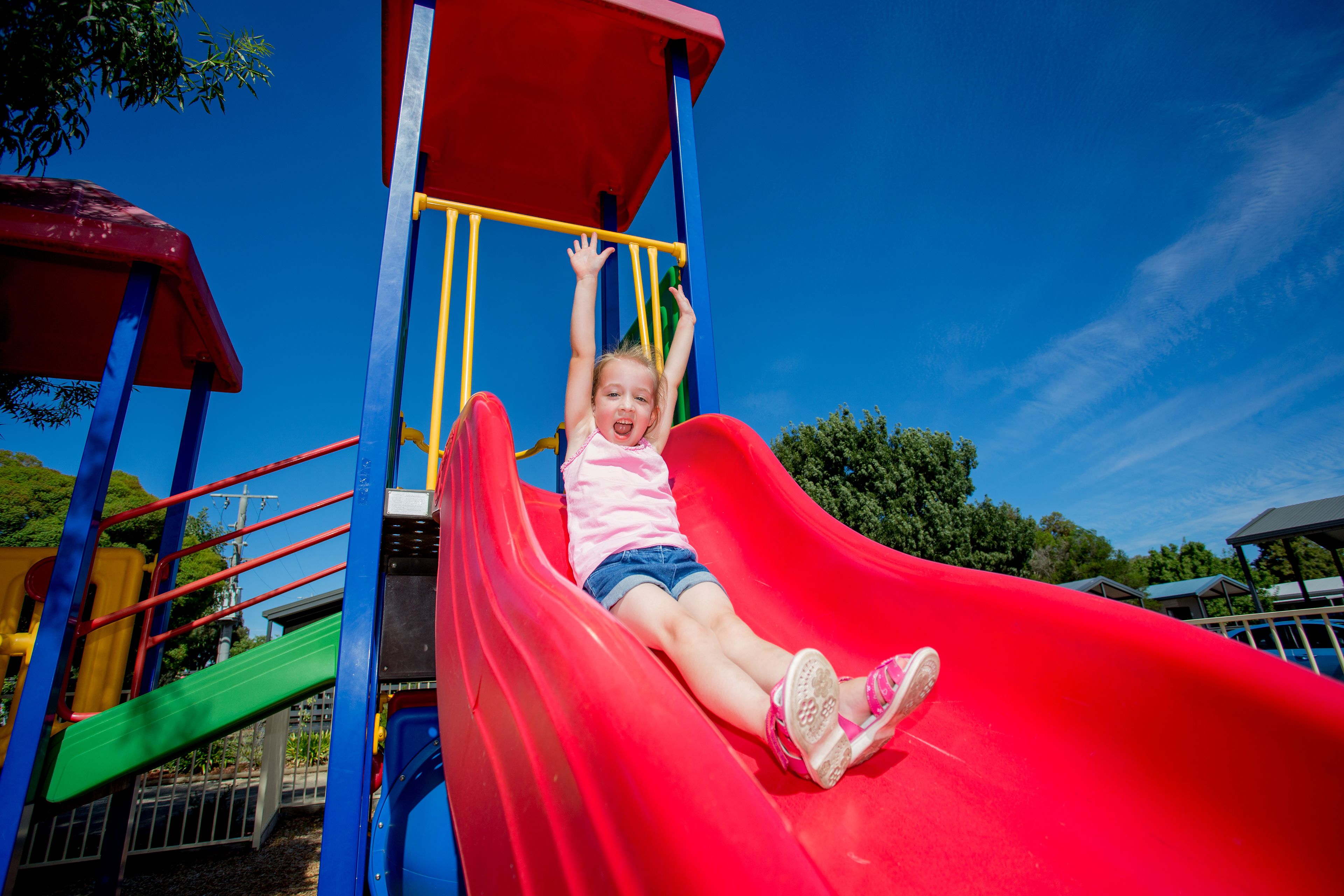 Un niño en un tobogán rojo en un parque infantil.