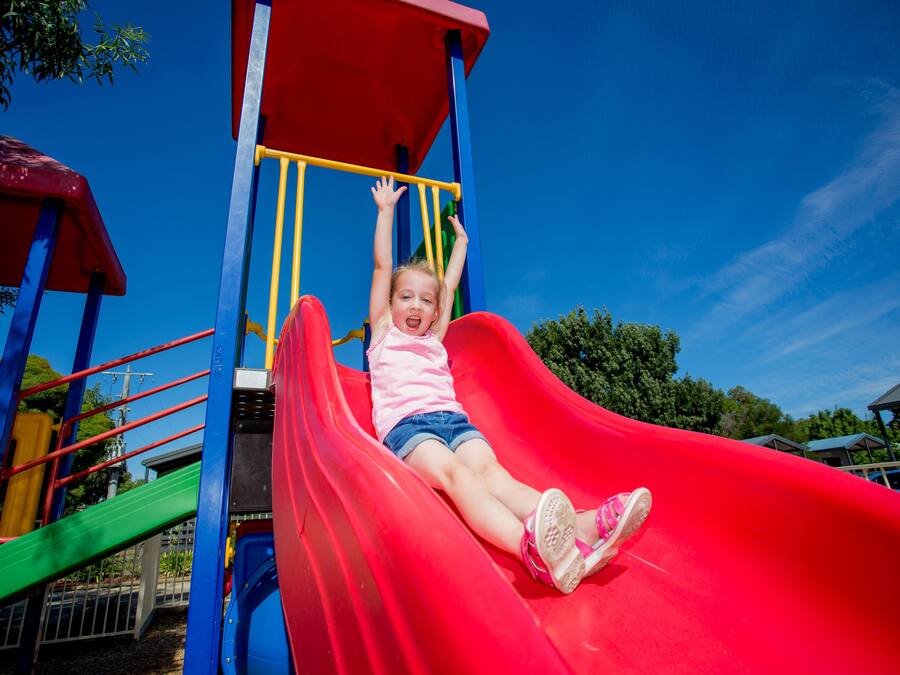 Un niño en un tobogán rojo en un parque infantil.
