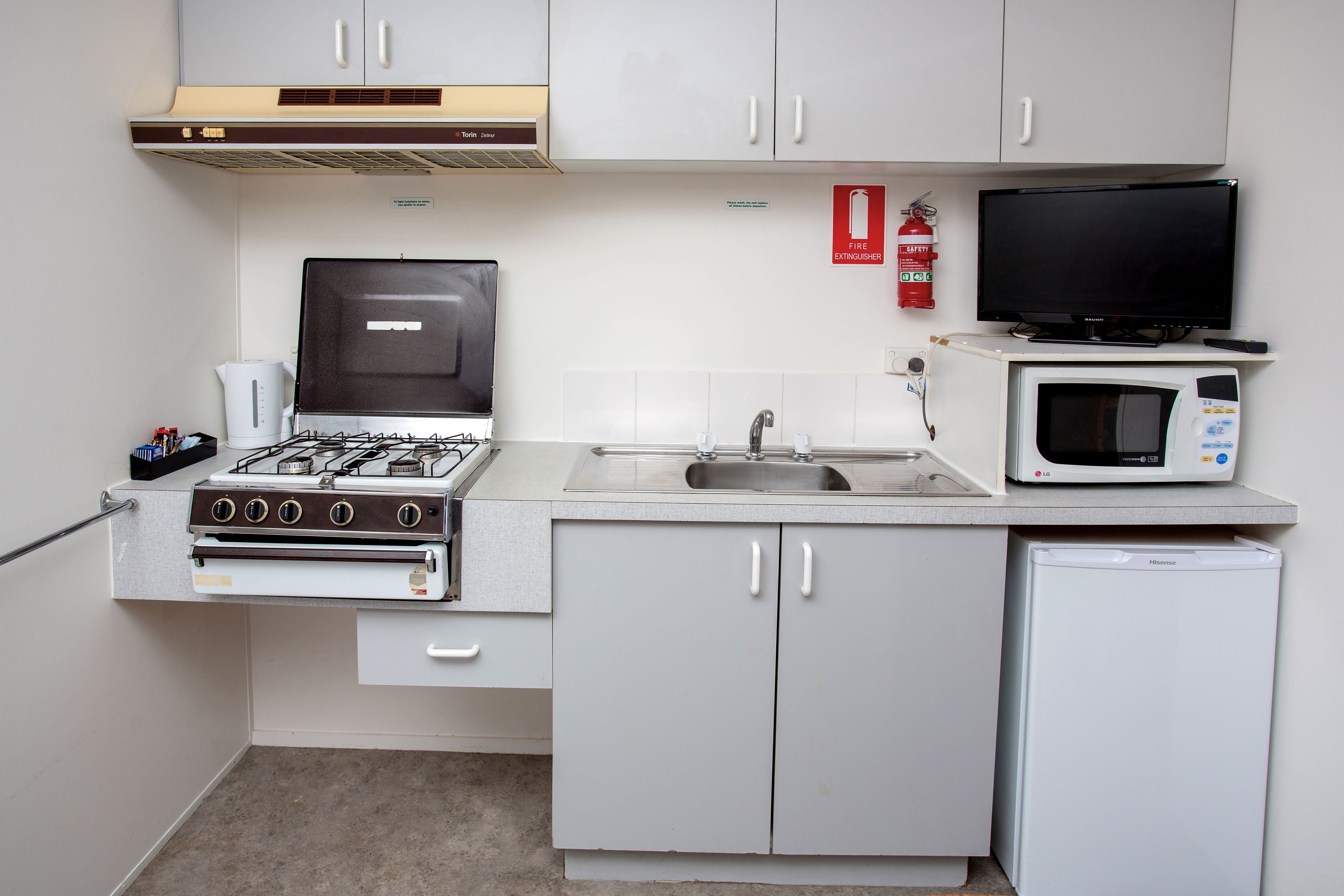 A compact kitchen with a gas stove, microwave, sink, and a small refrigerator.