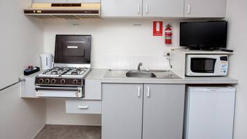 A compact kitchen with a gas stove, microwave, sink, and a small refrigerator.